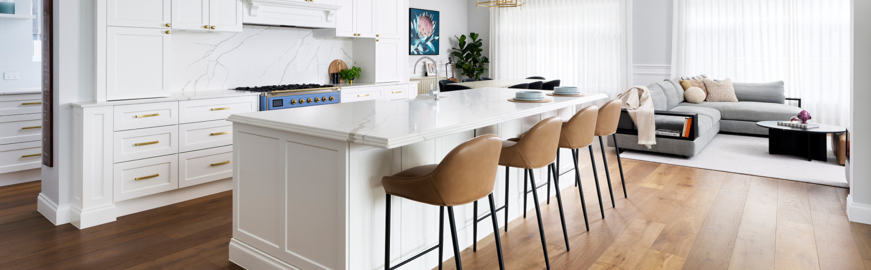 Light-filled kitchen at Lombardy Street featuring a long white island benchtop, timber bar stools and pendant lighting.