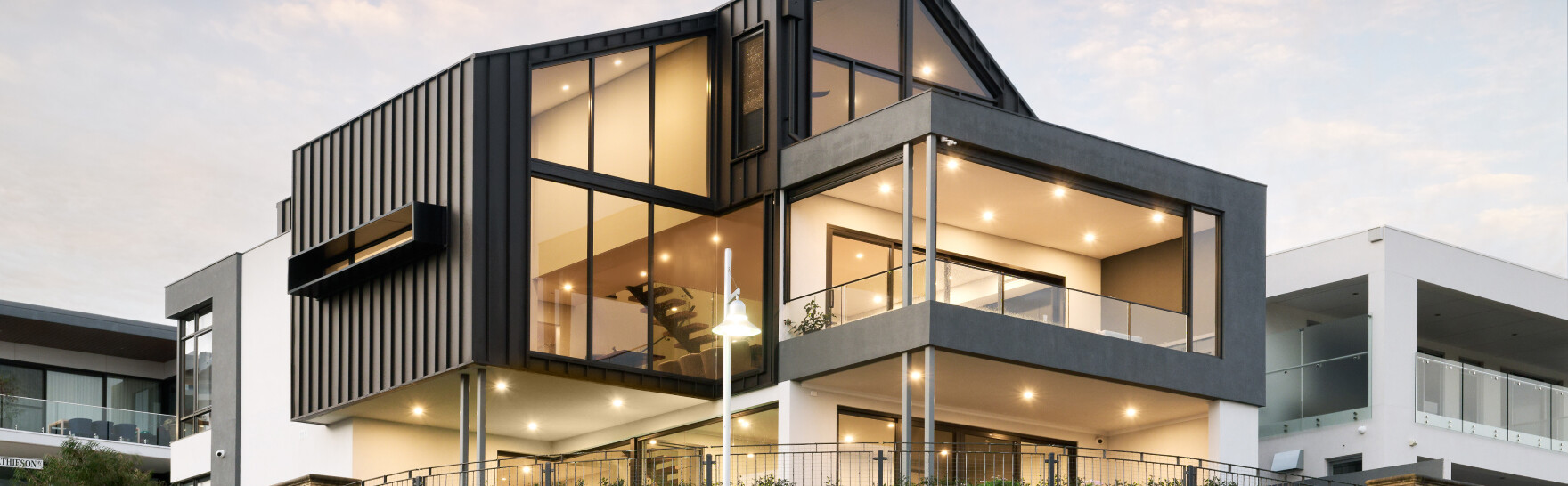 Three-storey custom home on Mathieson Avenue featuring dark vertical cladding, expansive glazing and covered balconies.