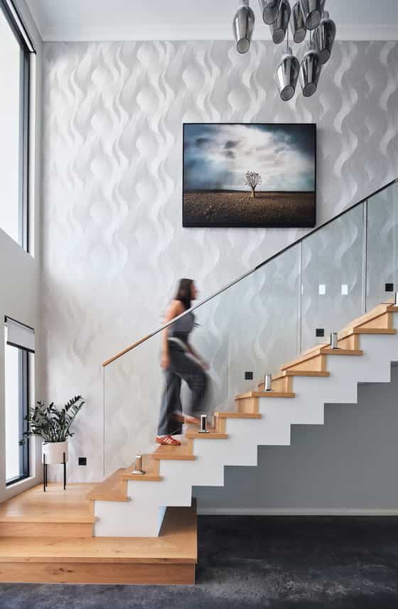 Floating timber staircase with glass balustrading, textured white walls and feature artwork in a custom home.