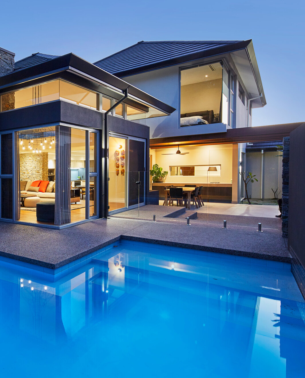 Two-storey custom home featuring a swimming pool, covered alfresco area and illuminated outdoor living spaces.